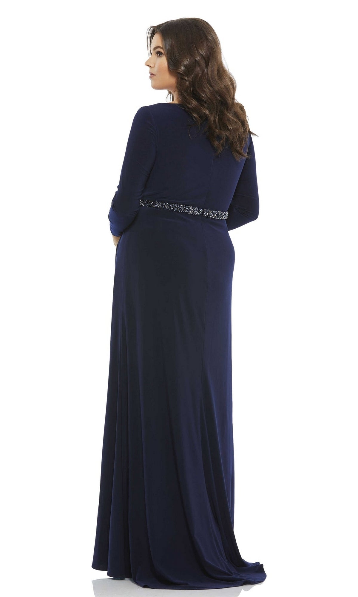 A woman stands facing away from the camera against a white background, wearing the Long Plus-Size Prom Dress 67899 by Mac Duggal—featuring long sleeves, a v-neckline, navy blue color, and decorative waist detail.